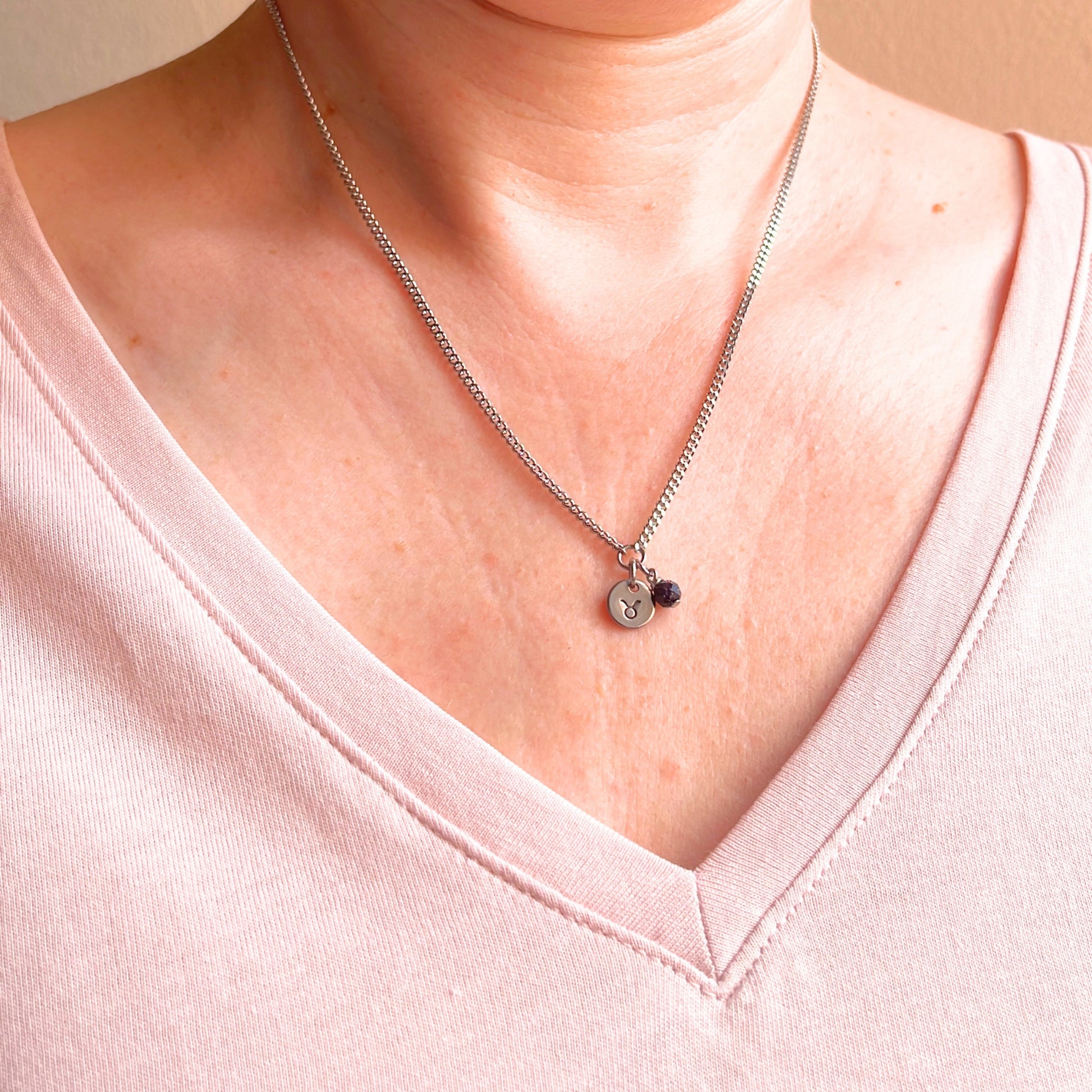 Woman wearing a pink v neck top and dainty Taurus zodiac sign necklace.