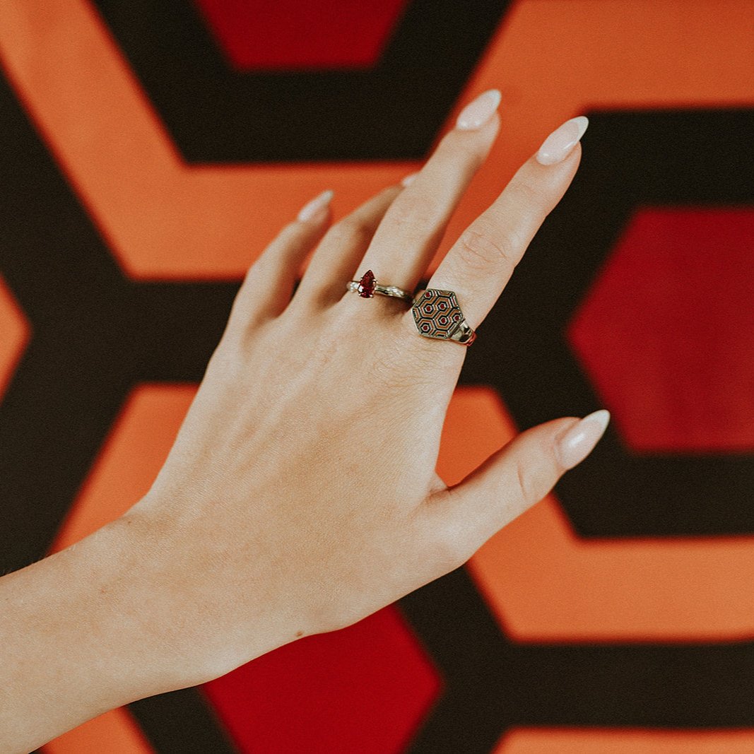 Hand wearing two rings with a geometric design against a red and black geometric background
