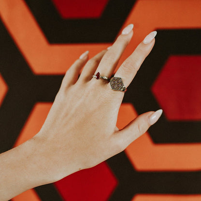 Hand wearing two rings with a geometric design against a red and black geometric background