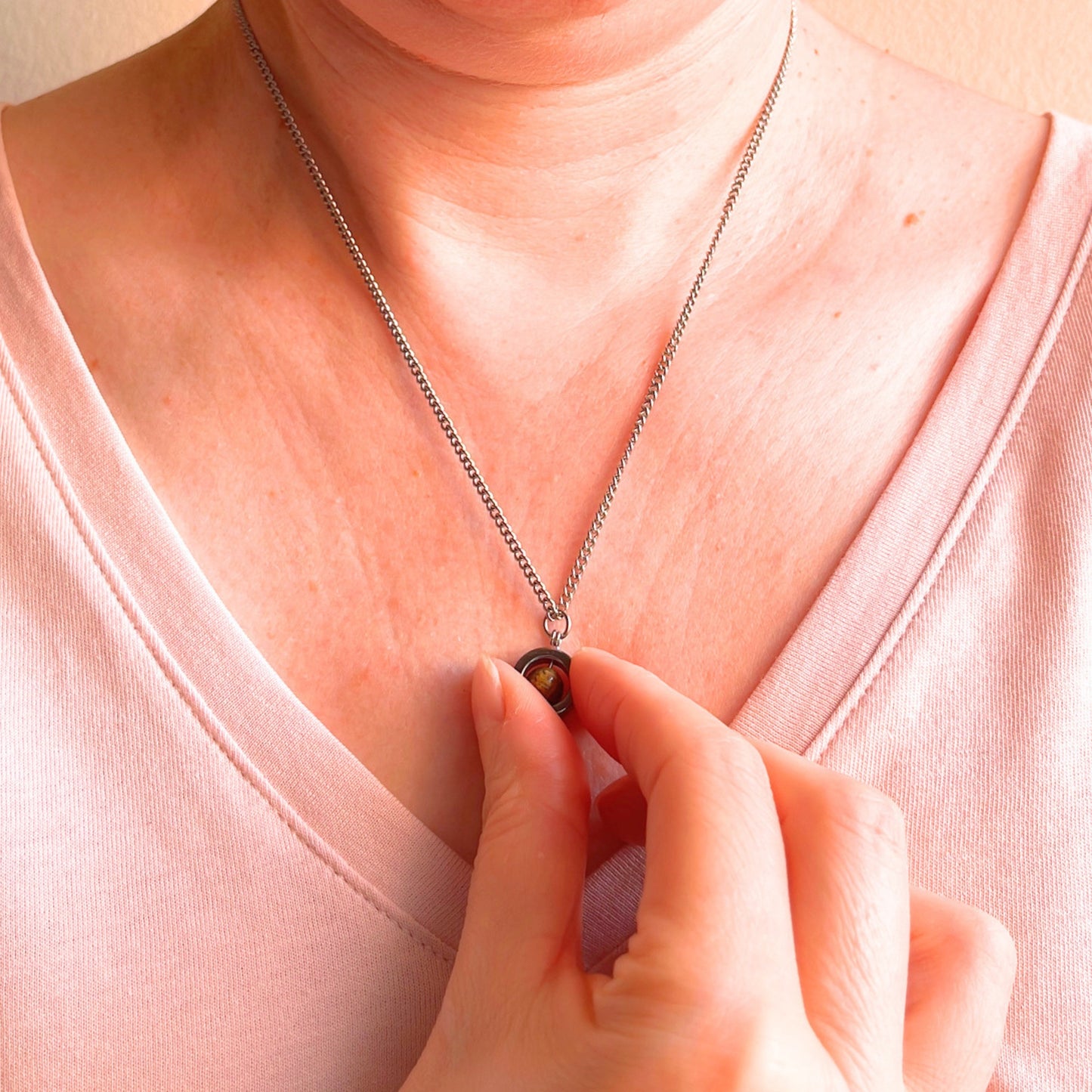 Close up of woman wearing silver chain and spinning pendant which she is holding in her hand.