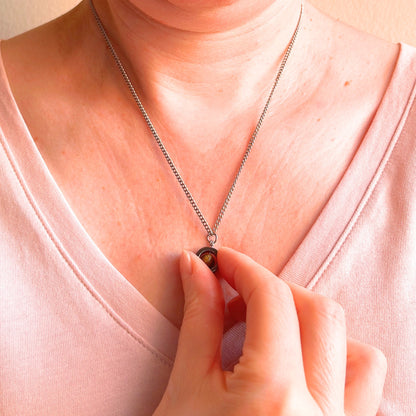 Close up of woman wearing silver chain and spinning pendant which she is holding in her hand.