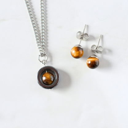 Tigers Eye spinner nacklace and stud earrings laying on a white marble background.