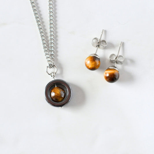 Tigers Eye spinner nacklace and stud earrings laying on a white marble background.