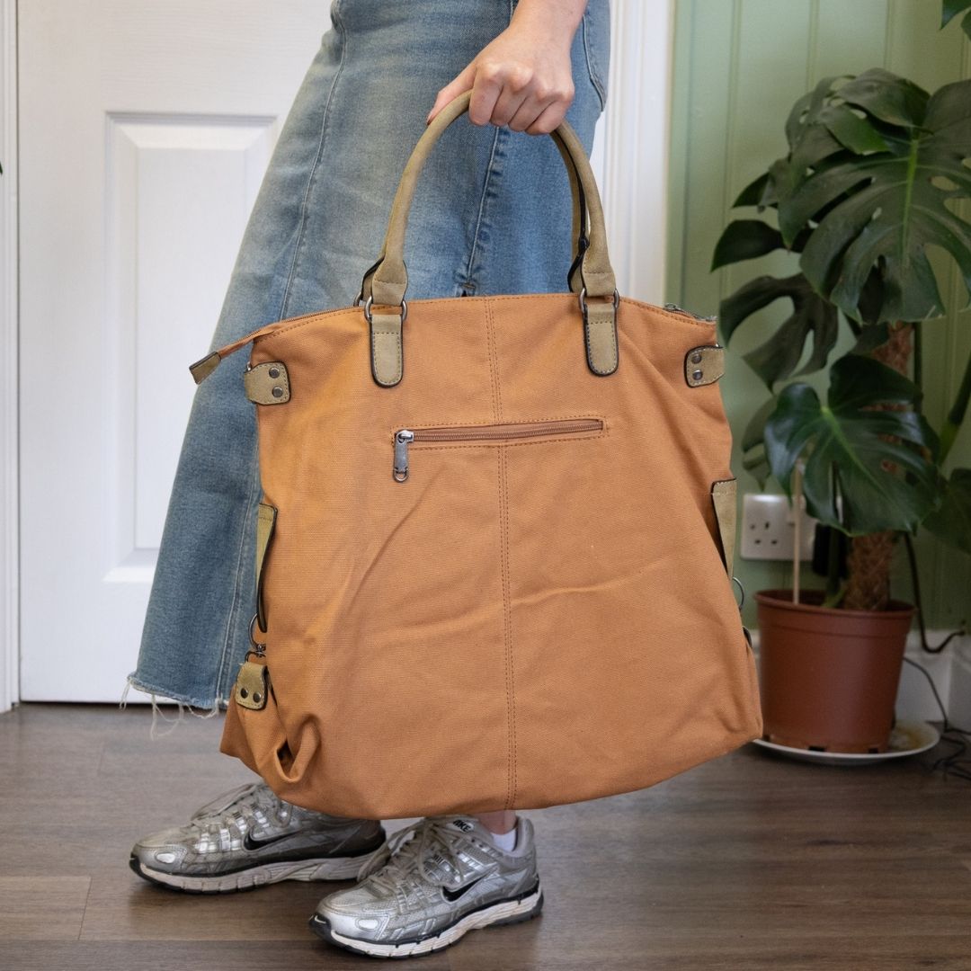 Person holding a brown tote bag indoors with a plant in the background