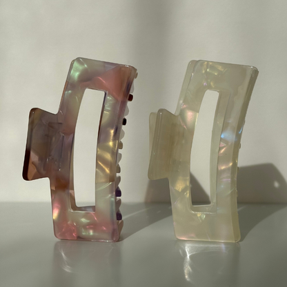 Two iridescent hair clips on a reflective surface with a neutral background