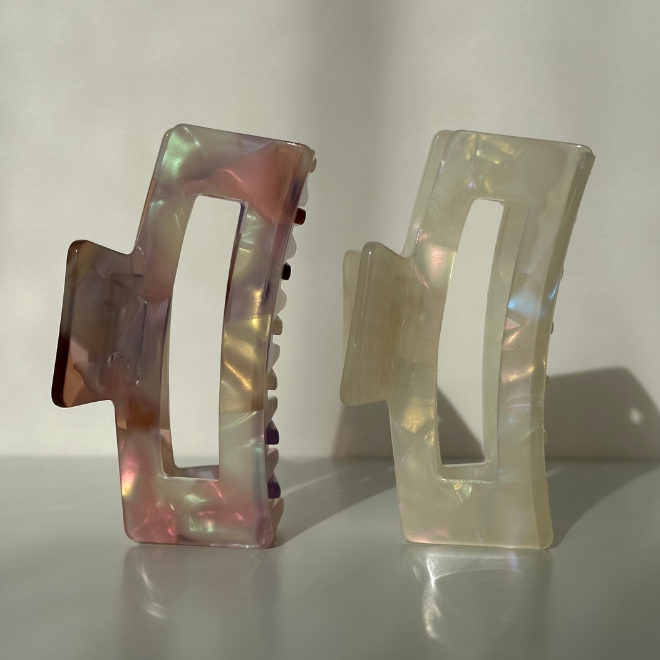 Two iridescent hair clips on a reflective surface with a neutral background