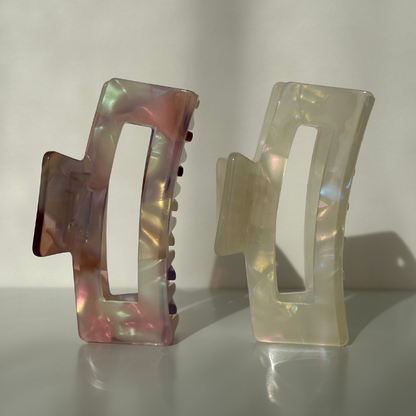 Two iridescent hair clips on a reflective surface with a neutral background