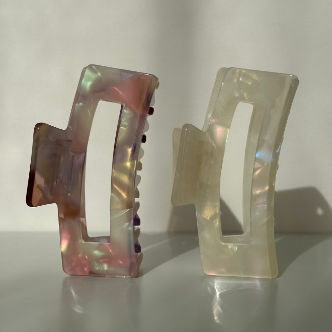 Two iridescent hair clips on a reflective surface with a neutral background