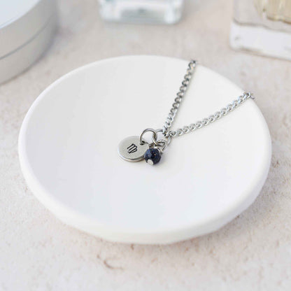 Tiny Virgo zodiac sign disc pendant necklace with Blue Goldstone charm laying on white trinket dish