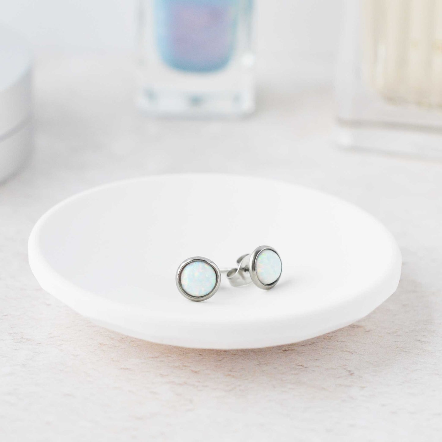 Pair of silver earrings with a light-colored gemstone on a white dish.