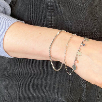 Pale woman wearing three chain bracelets one of which has small charms dangling from it.