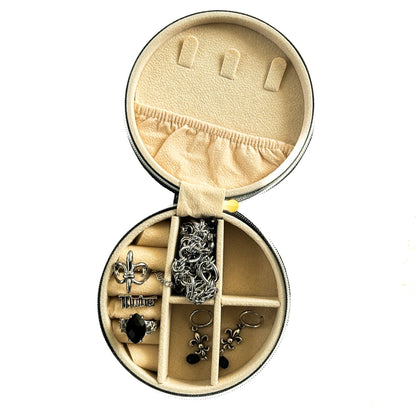 Round jewelry box with compartments containing various earrings on a white background