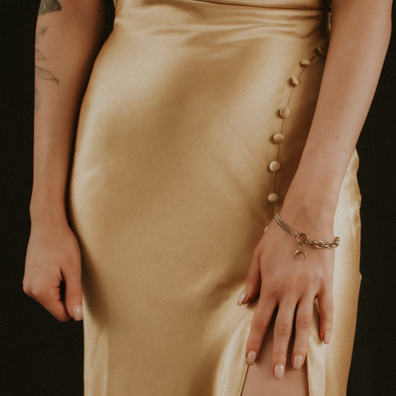 Close-up of a person wearing a gold dress with buttons and a bracelet on a dark background