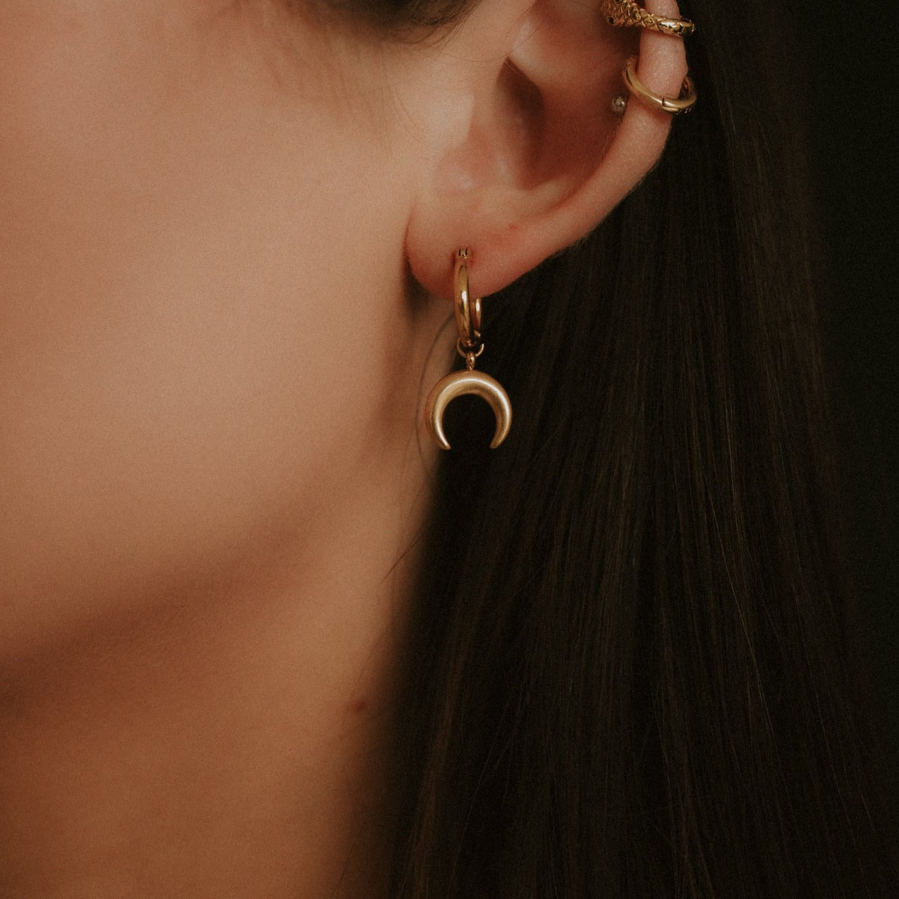 Close-up of an ear wearing a gold hoop earring with a crescent moon charm.
