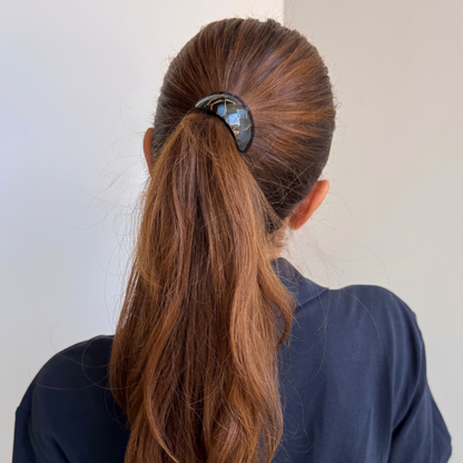 Person with long brown hair tied in a ponytail wearing a dark blue shirt against a light background