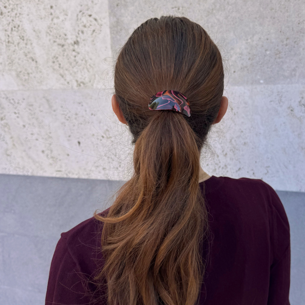 Person with long brown hair in a ponytail wearing a maroon sweater against a light stone wall.