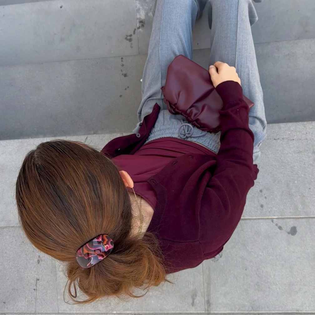 Person sitting on a concrete step with a maroon jacket and gray pants.