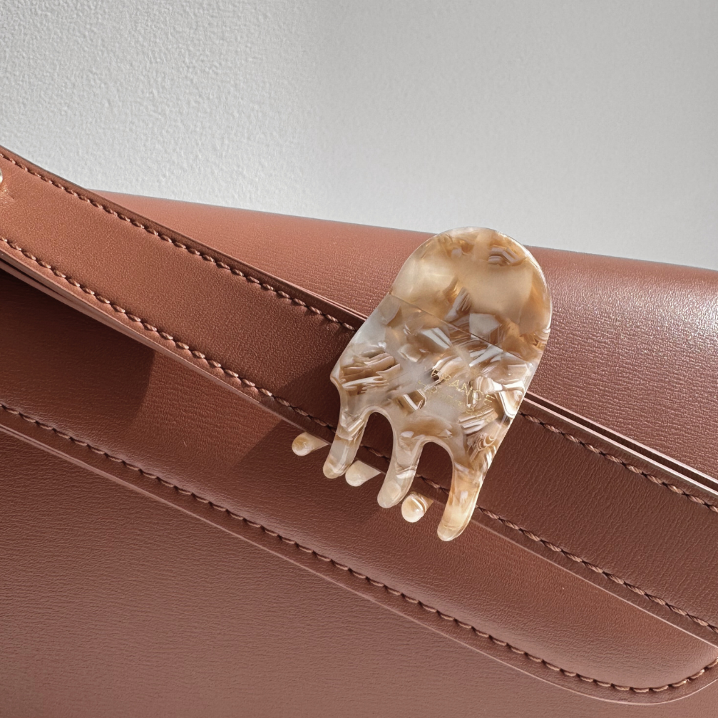 Brown handbag with a decorative hair clip on a neutral background