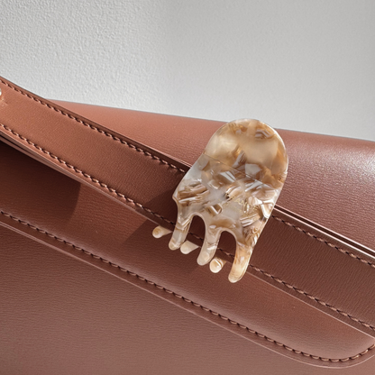 Brown handbag with a decorative hair clip on a neutral background