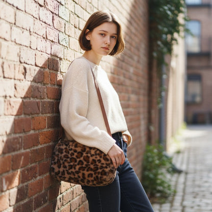 Woman leaning against a brick wall holding a faux fub bag in an urban setting