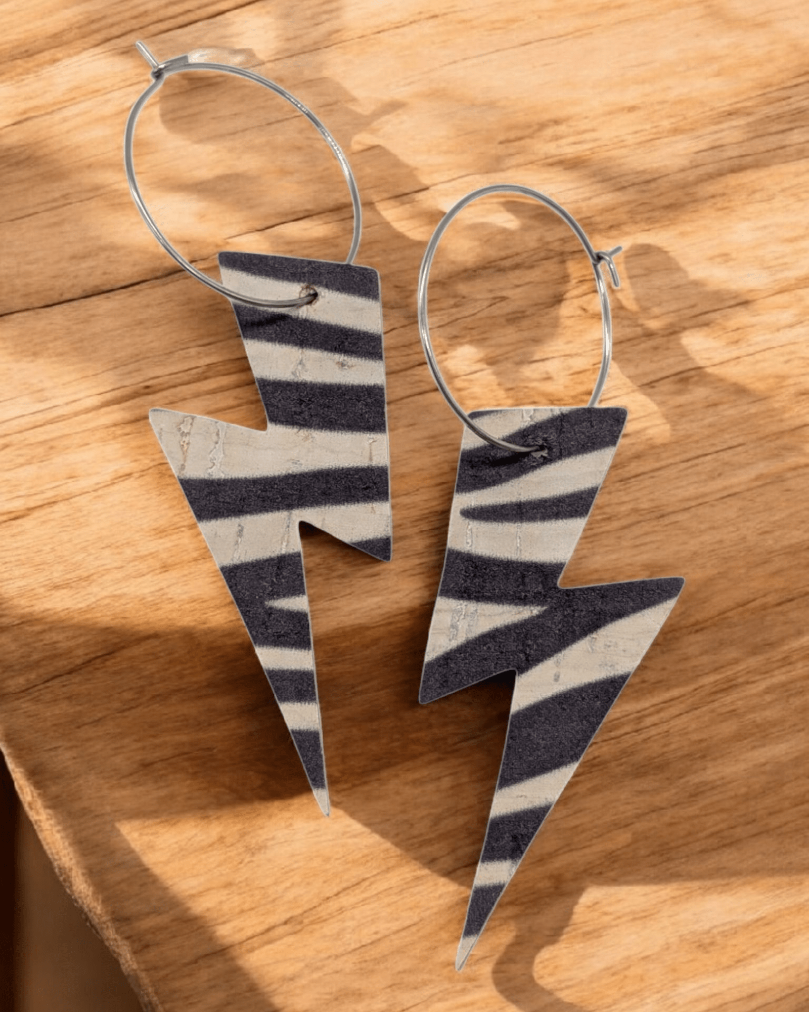 Zebra print lightning bolt hoop earrings laying on a wood table top.