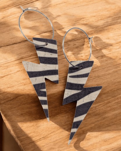 Zebra print lightning bolt hoop earrings laying on a wood table top.