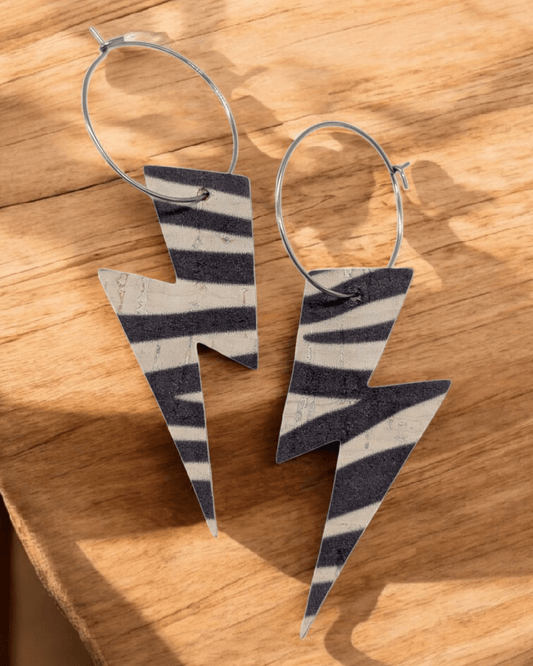 Zebra print lightning bolt hoop earrings laying on a wood table top.
