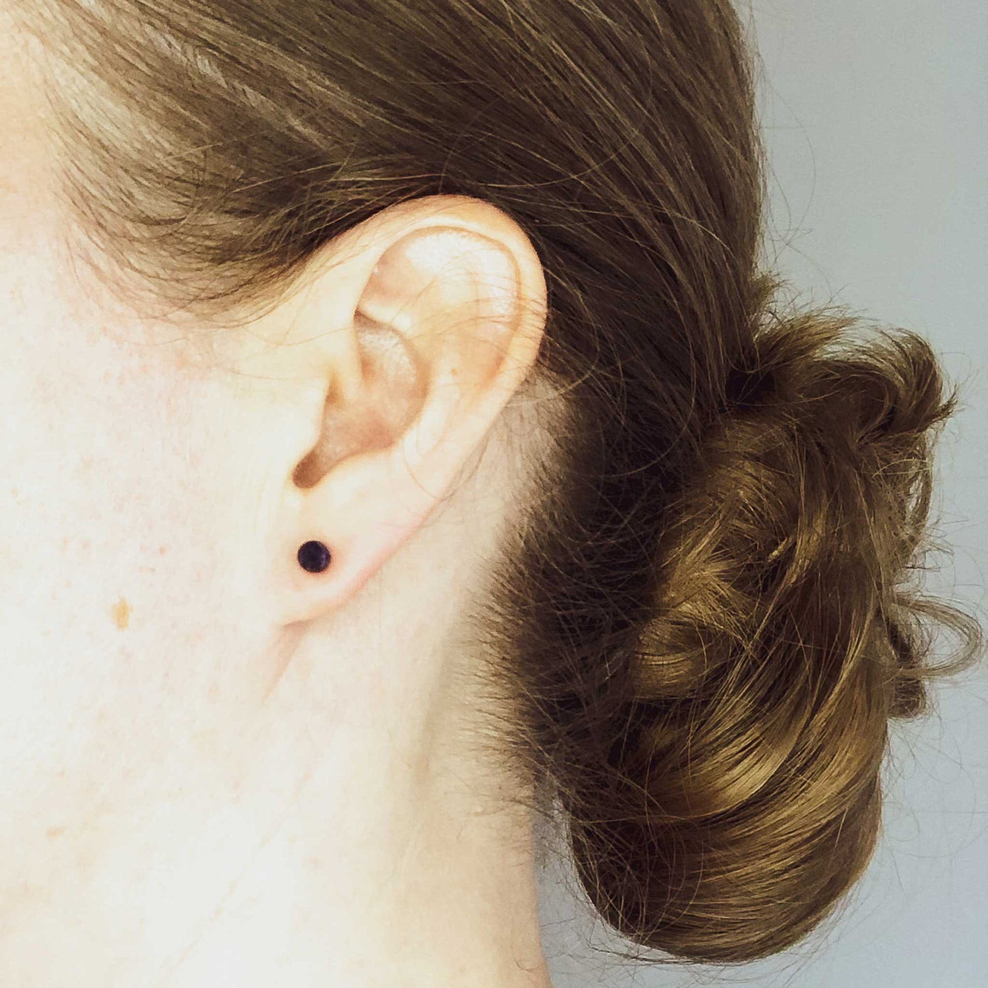 Woman wearing small blue stud earring in earlobe