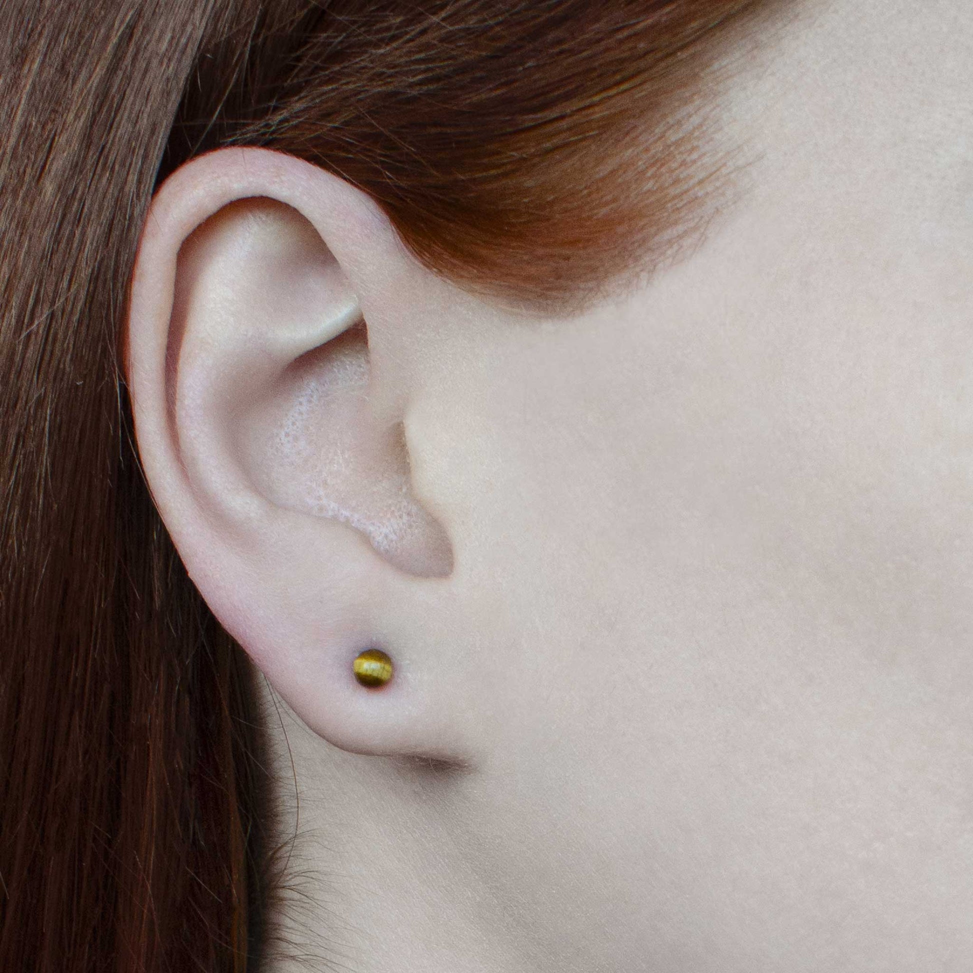 Woman wearing small tigers eye stud earring in earlobe