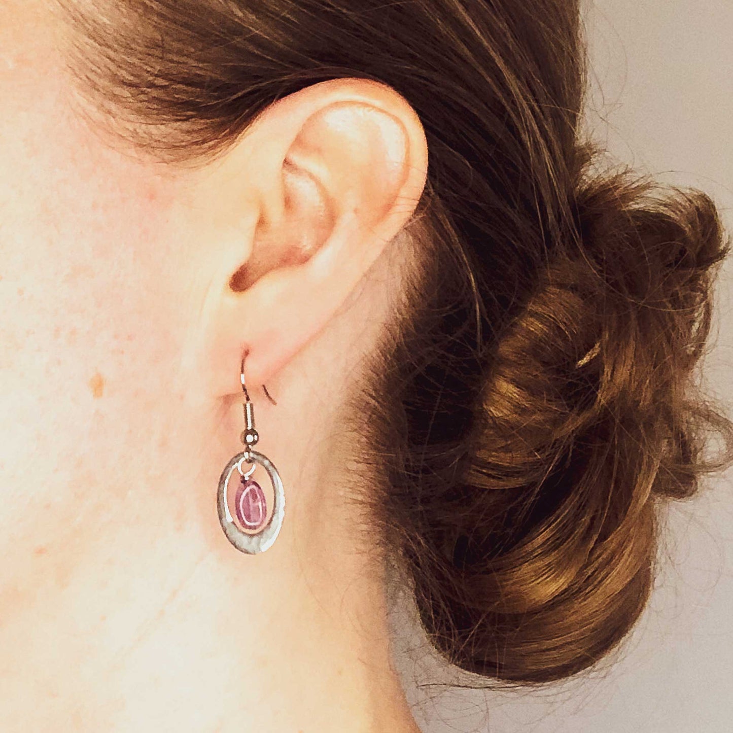 Woman wearing oval Amethyst drop earrings.