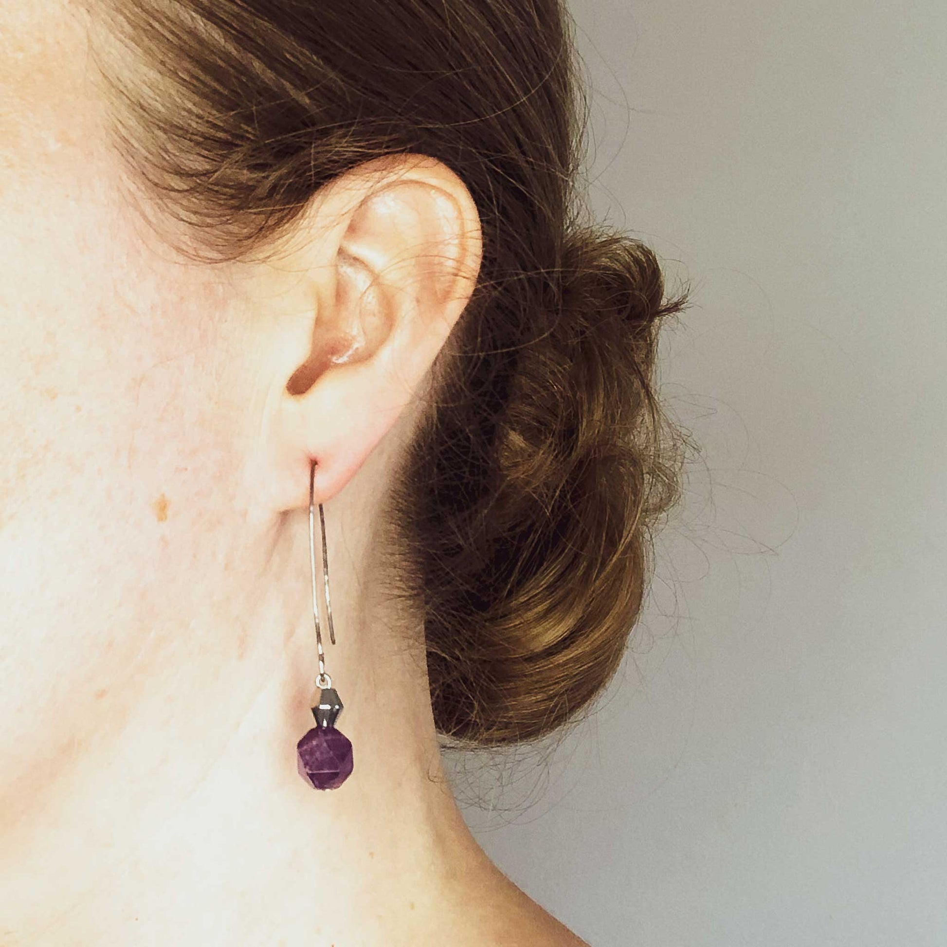 Woman wearing long Amethyst drop earrings.