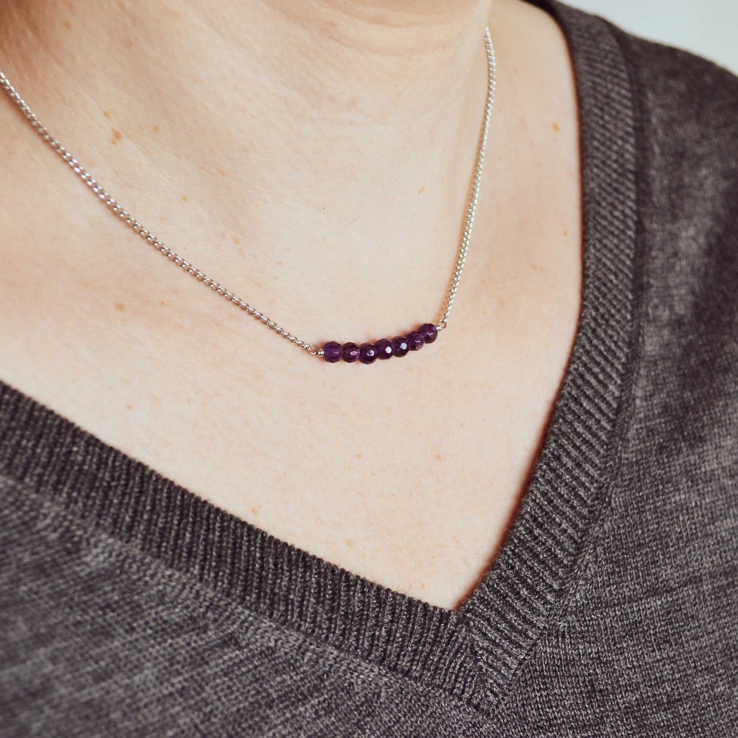 Woman wearing grey v neck jumper and dainty purple Amethyst necklace
