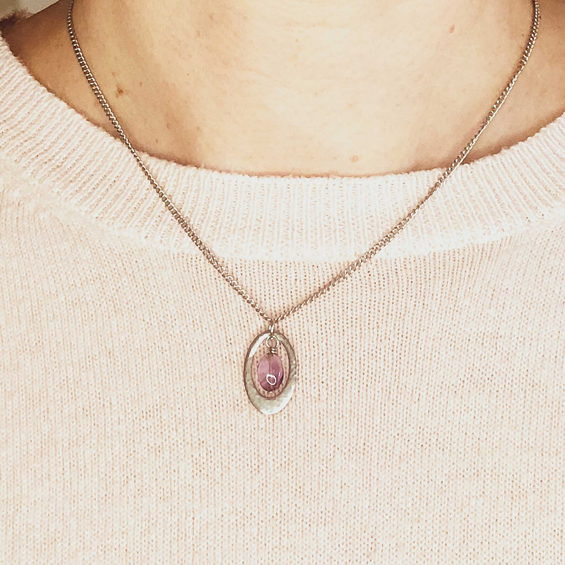 Woman wearing pink jumper and oval shaped Amethyst pendant necklace.