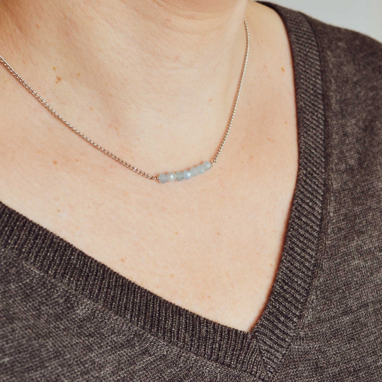 Woman wearing grey v neck jumper and dainty Aquamarine necklace