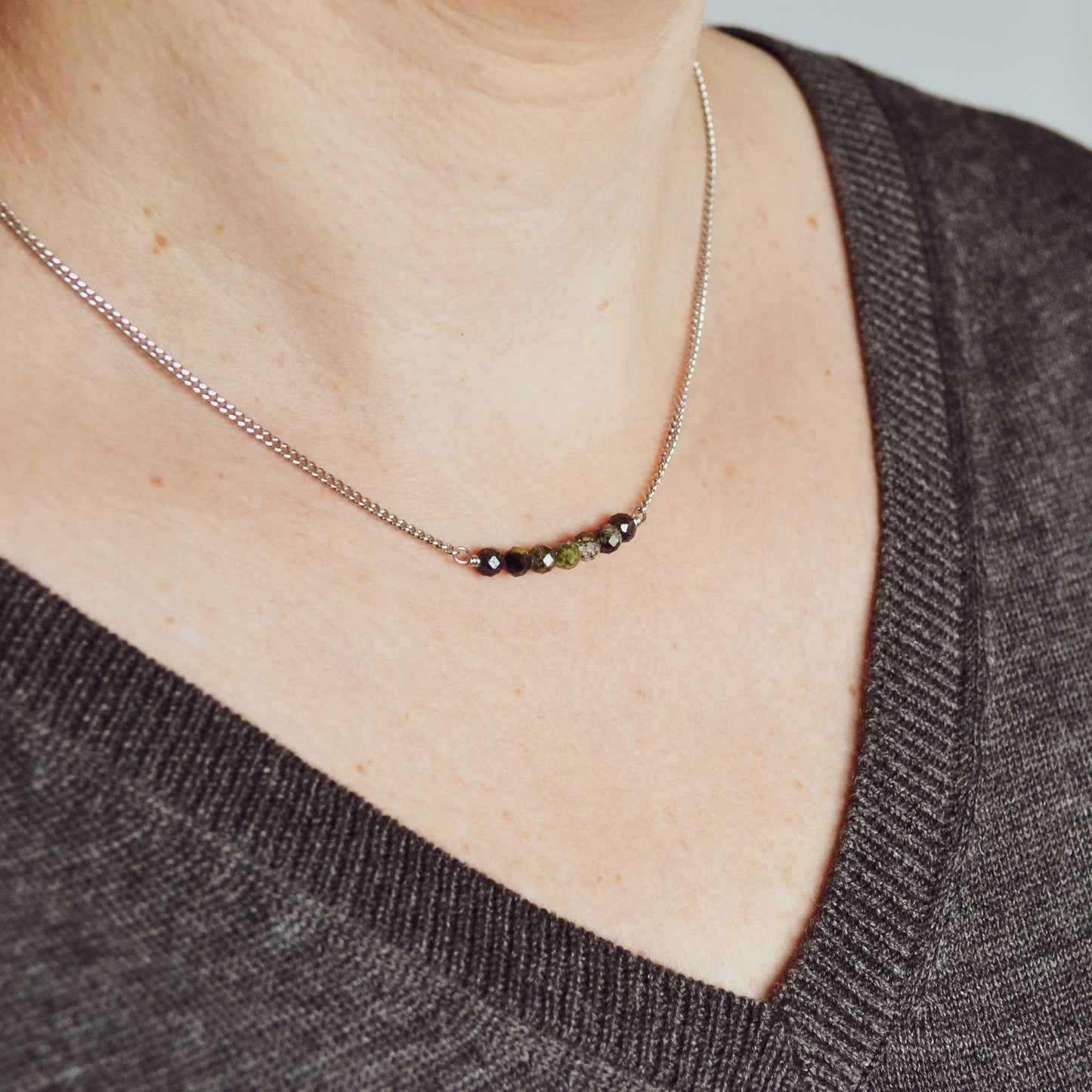 Woman wearing grey v neck jumper and dainty dark green stone necklace