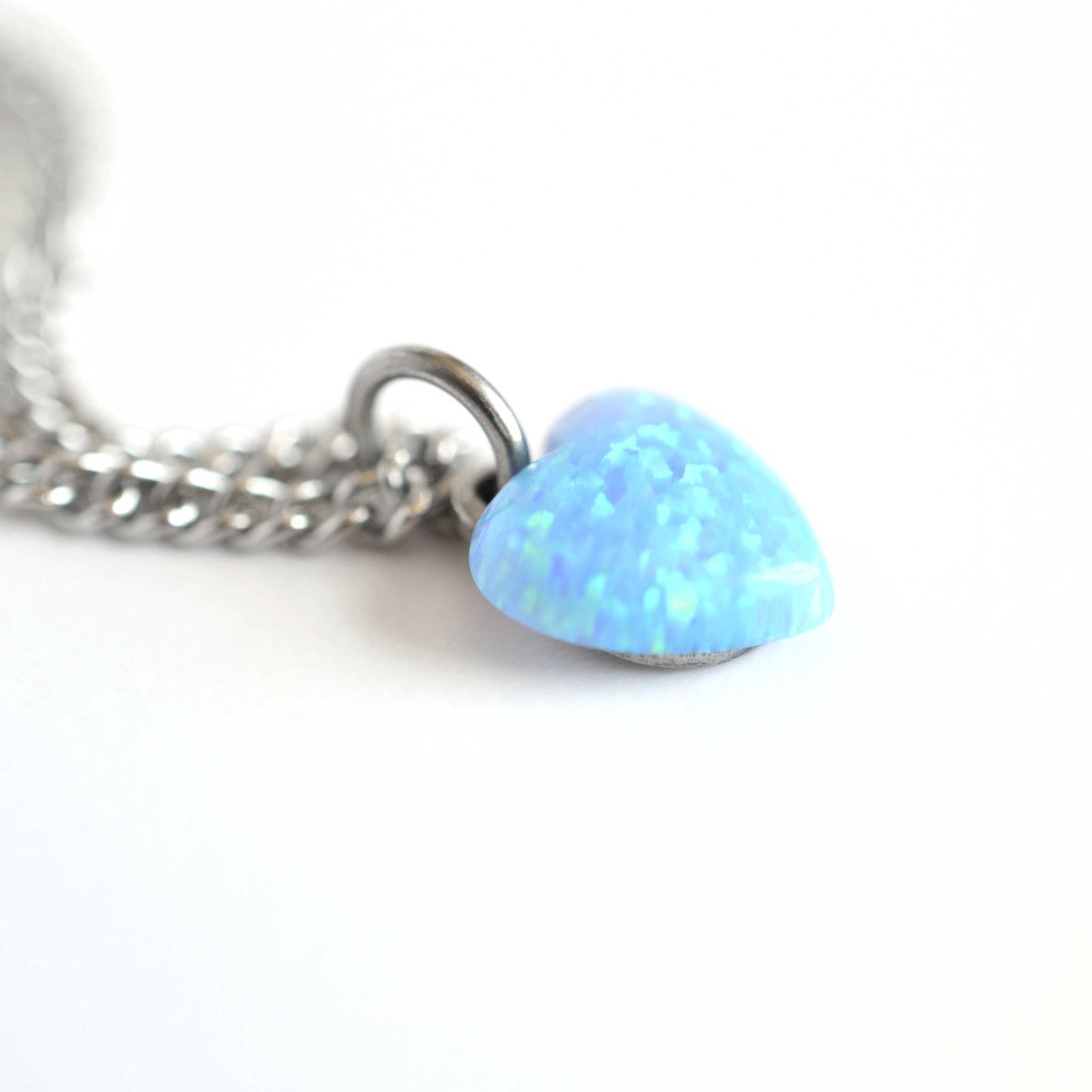 Close up of blue lab created Opal heart pendant hanging from stainless steel chain