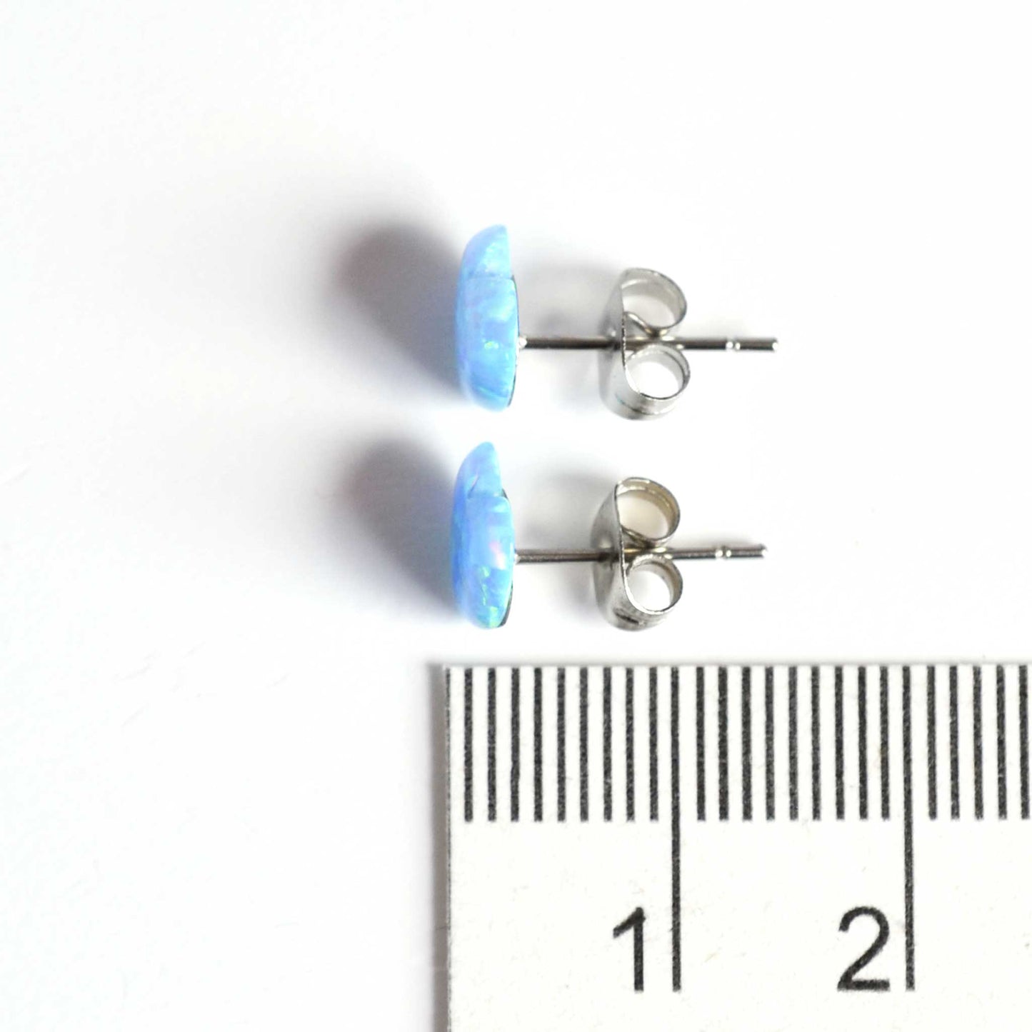 8mm blue opal heart stud earrings next to ruler