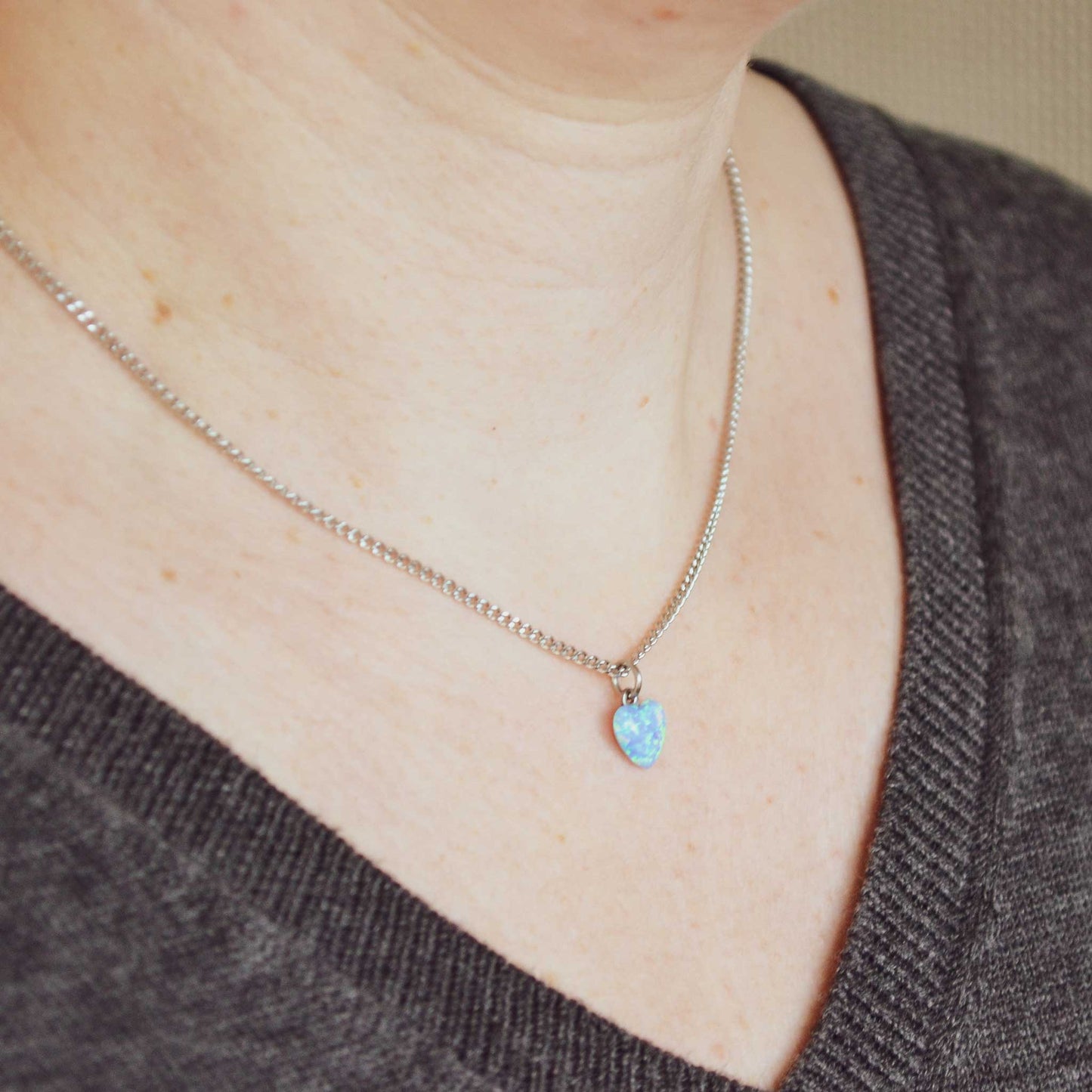 Woman wearing grey v neck jumper and dainty blue heart pendant necklace