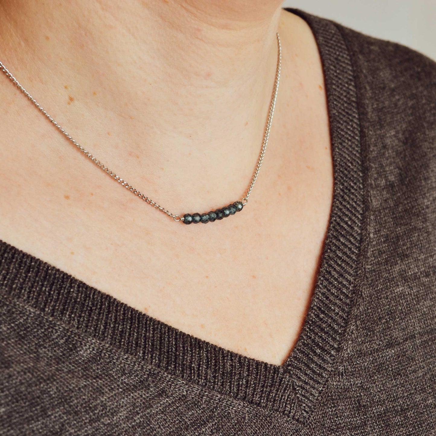 Woman wearing grey v neck jumper and dainty blue Topaz necklace