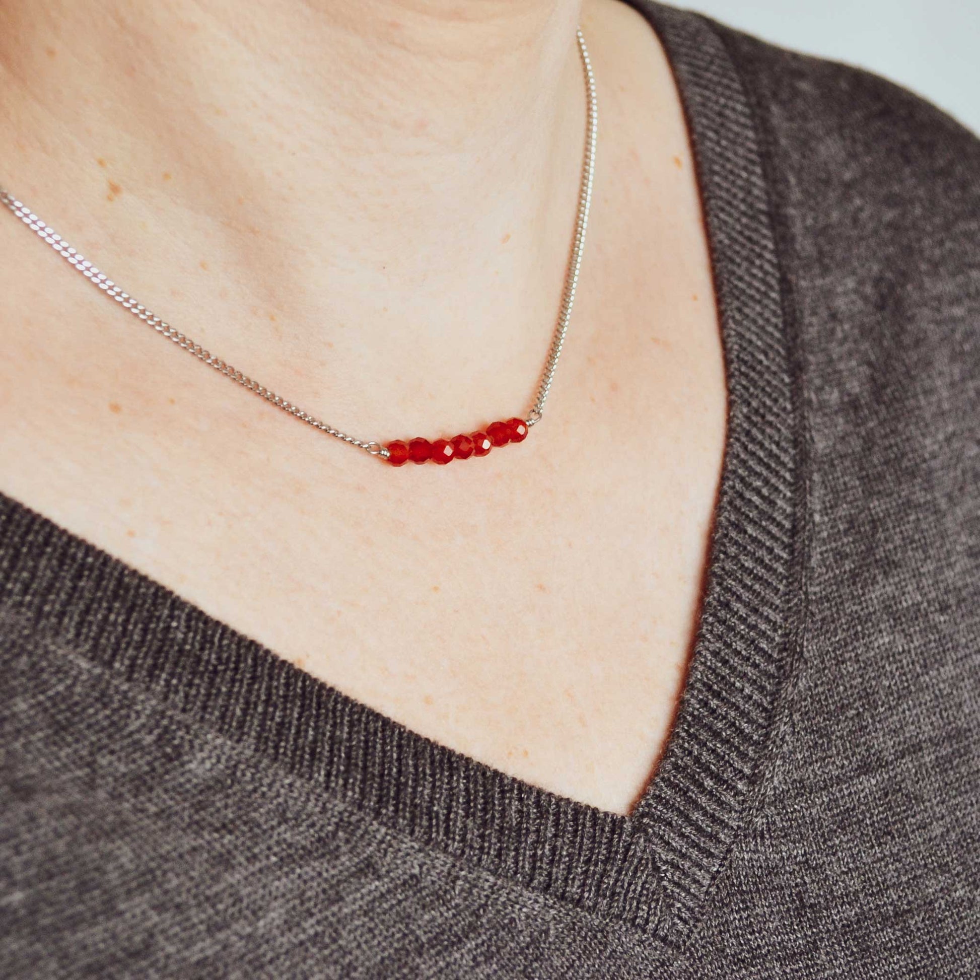 Woman wearing grey v neck jumper and dainty Carnelian necklace