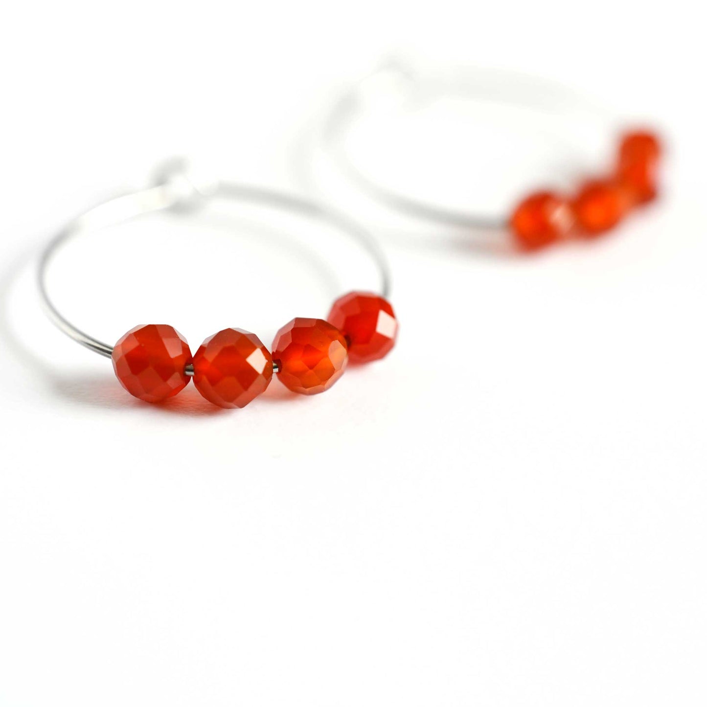 Close up of Carnelian hoop earrings with four small round faceted orange Carnelian gemstones