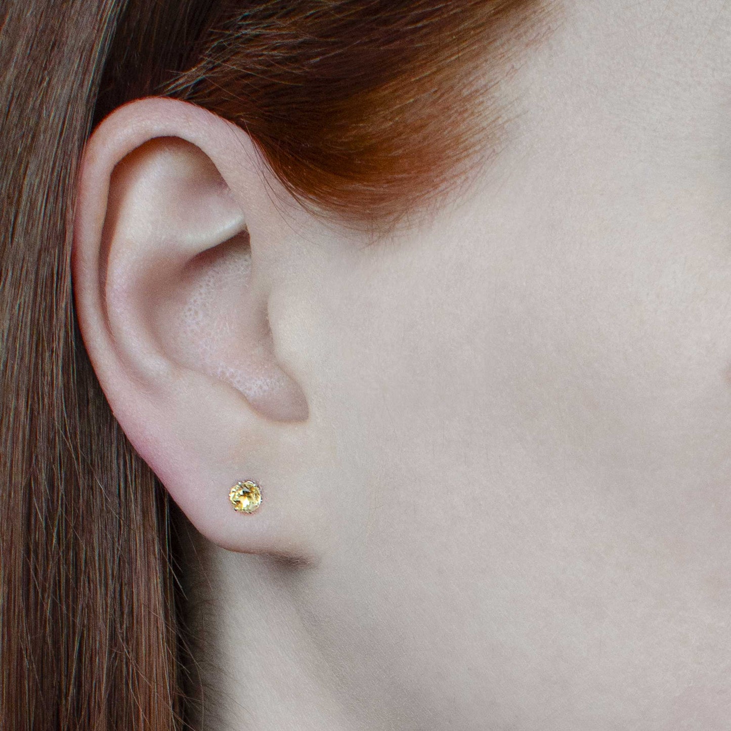 Woman wearing tiny yellow Citrine stud earrings in earlobe