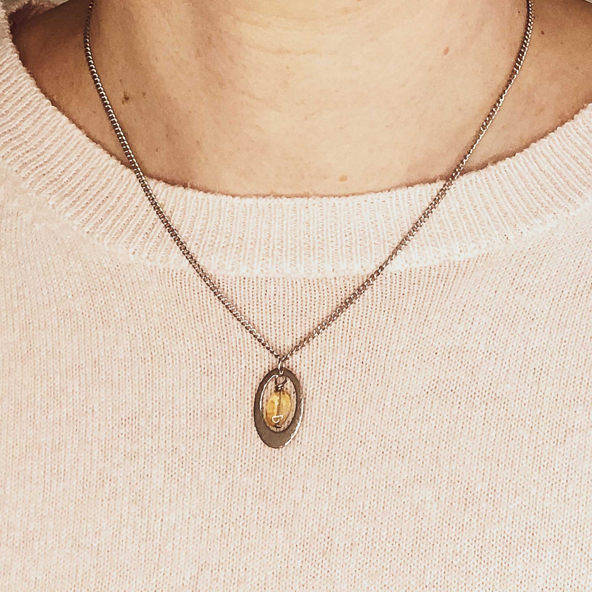 Woman wearing pink jumper and dainty oval Citrine pendant necklace.