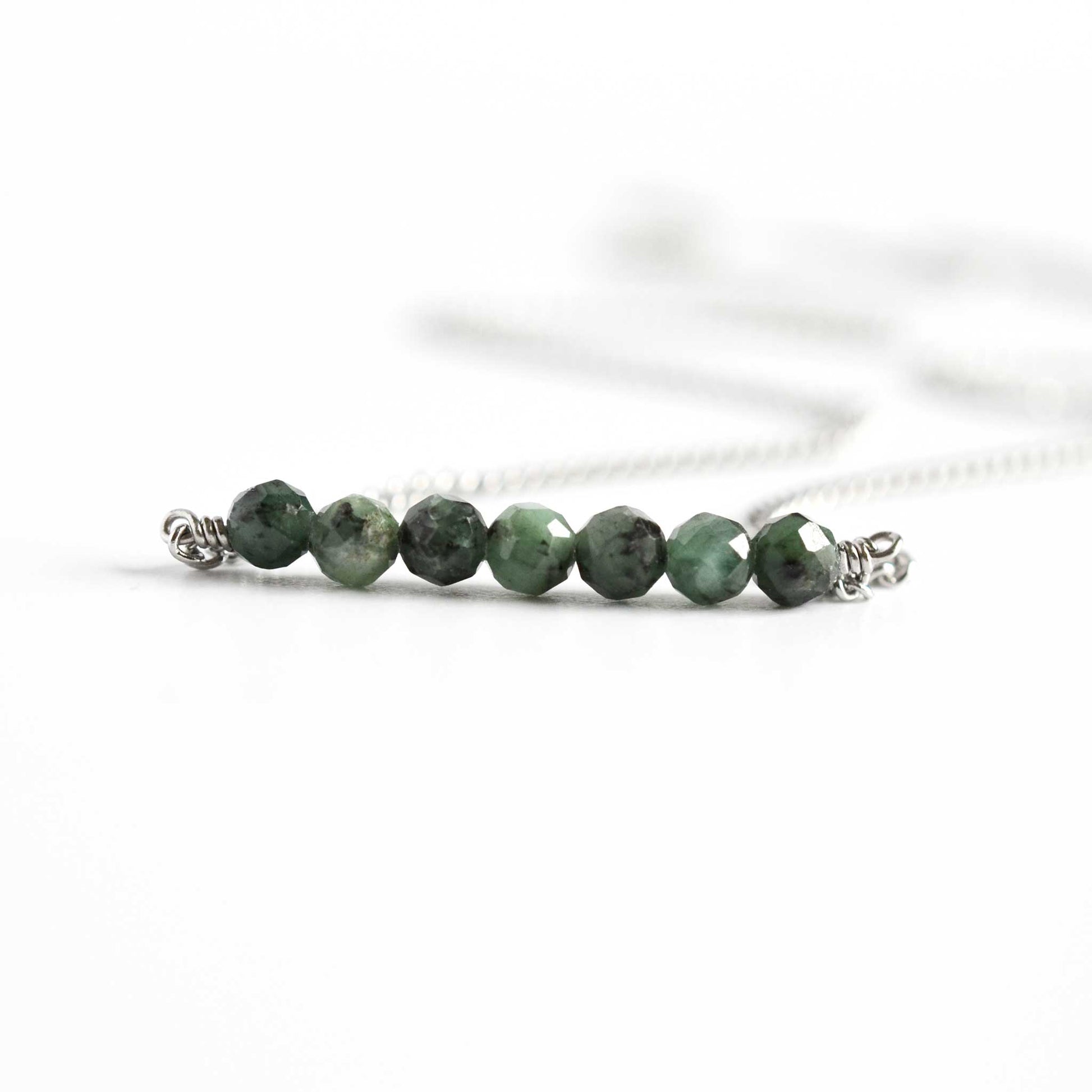 Close up of dainty necklace with seven small round faceted dark green Emerald gemstone beads