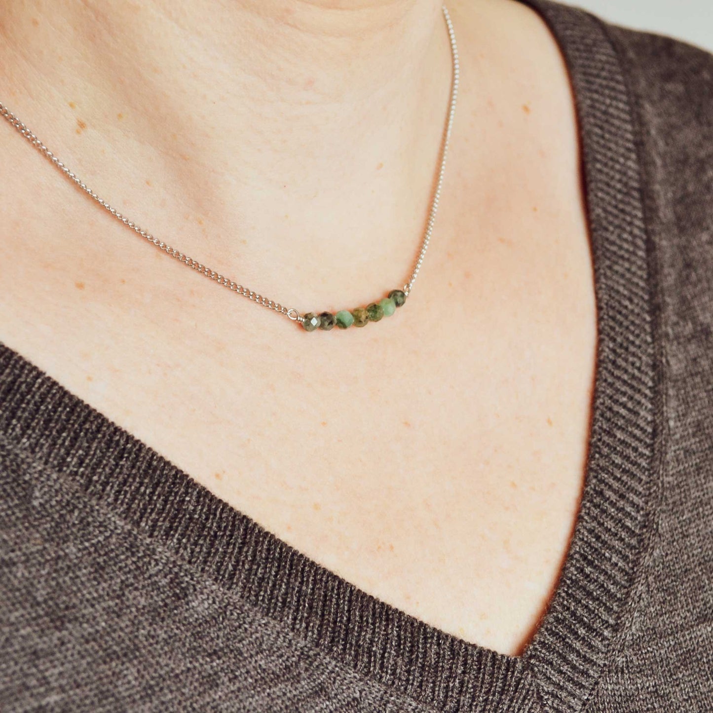 Woman wearing grey v neck jumper and dainty necklace with Emerald stones