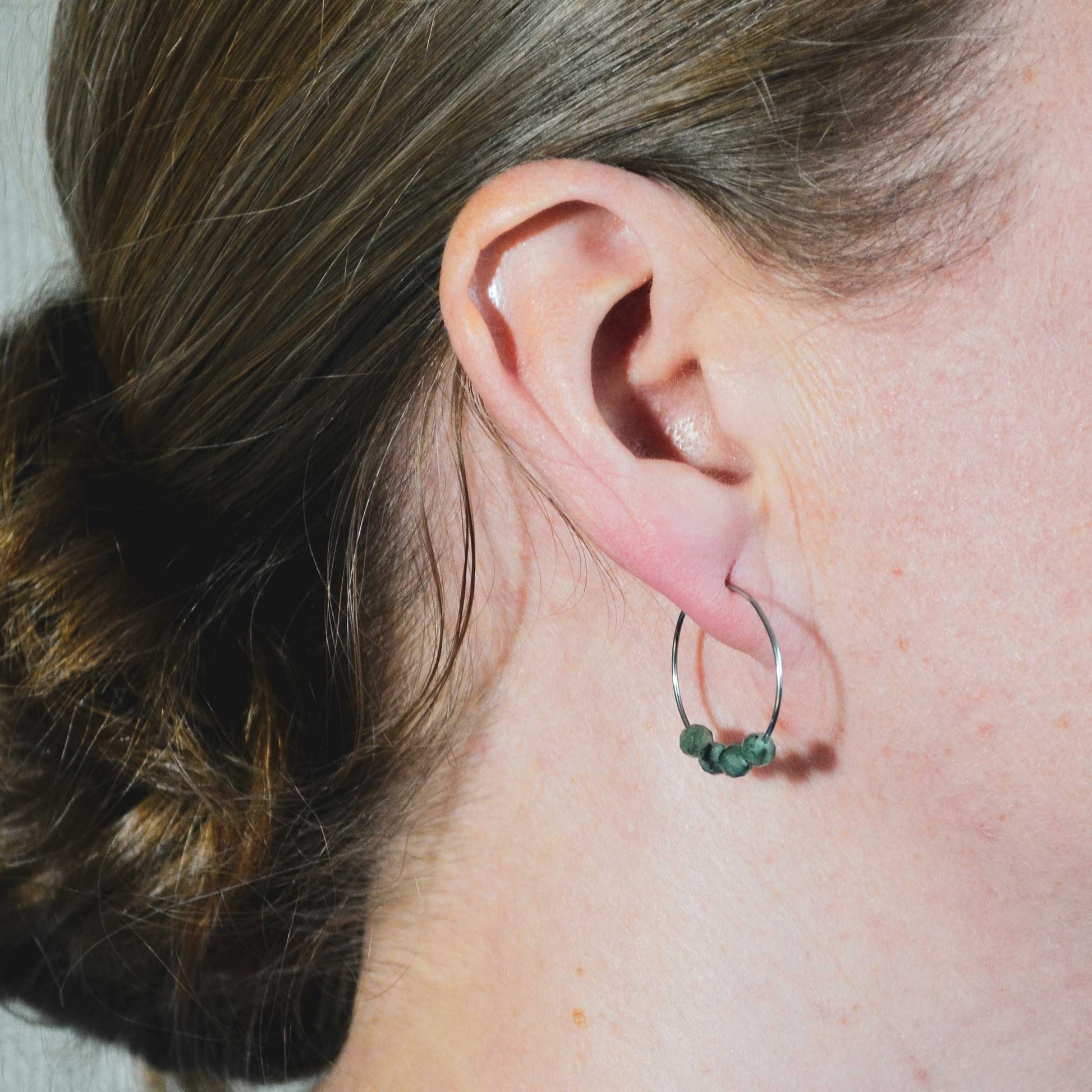 Woman wearing dark green Emerald hoop earrings in earlobe