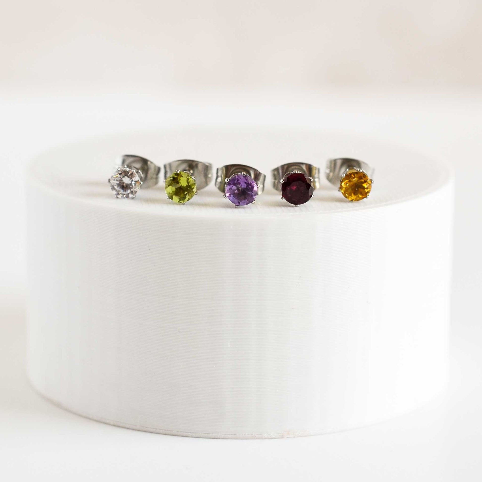 Five different coloured gemstone stud earrings sitting on a round white plinth