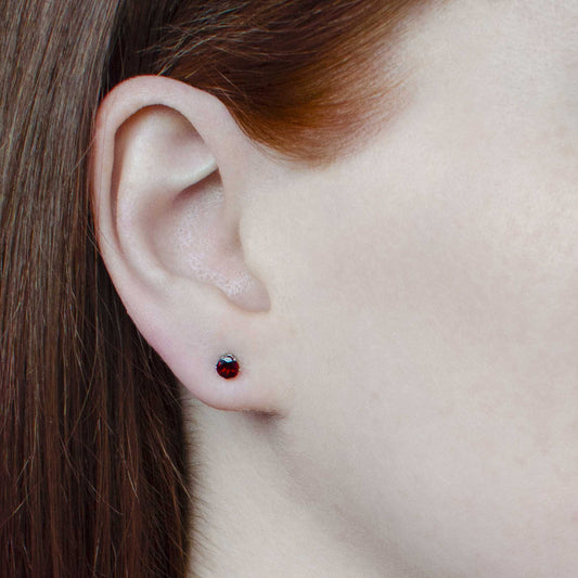 Woman wearing tiny dark red Garnet stud earrings in earlobe
