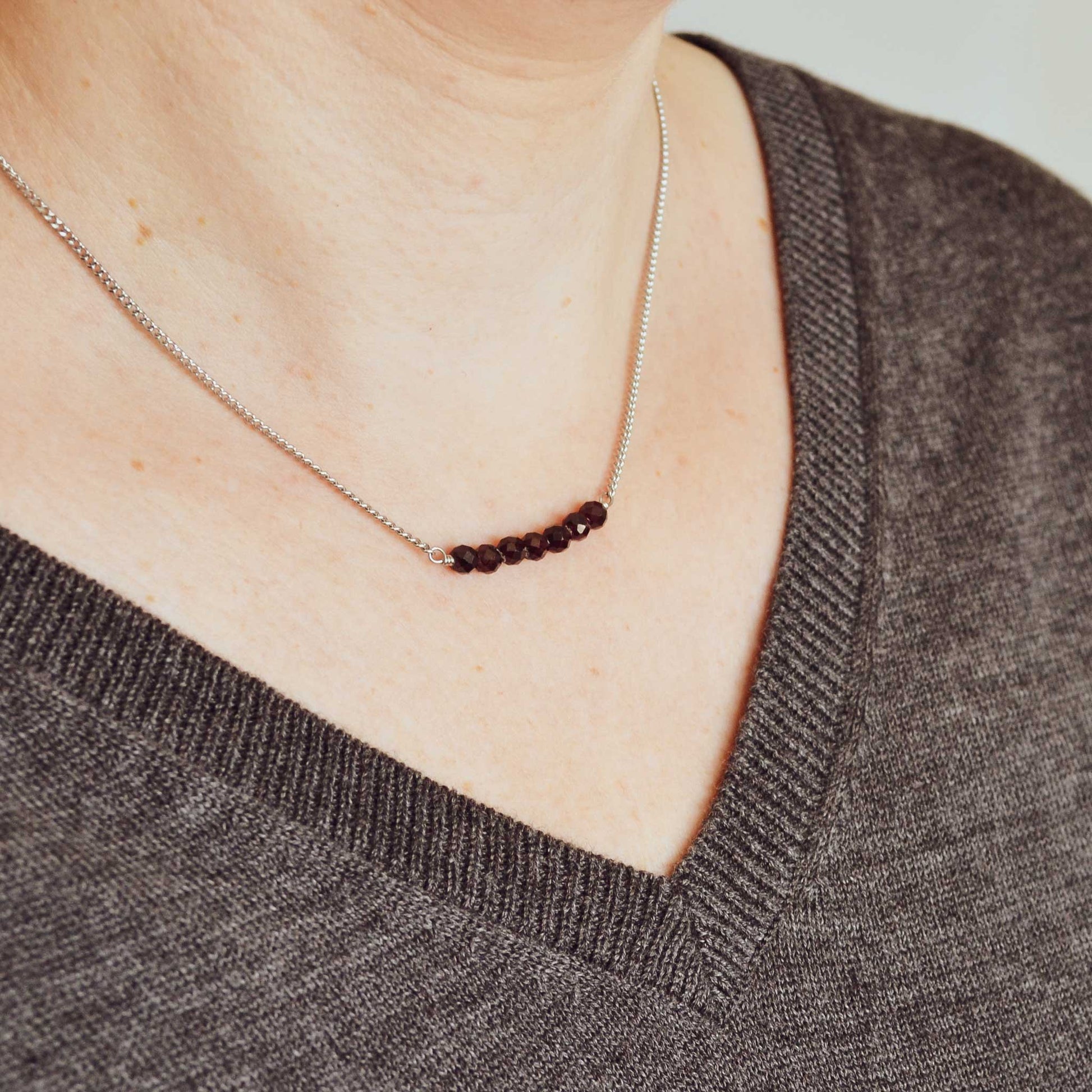 Woman wearing grey v neck jumper and dainty Garnet crystal necklace