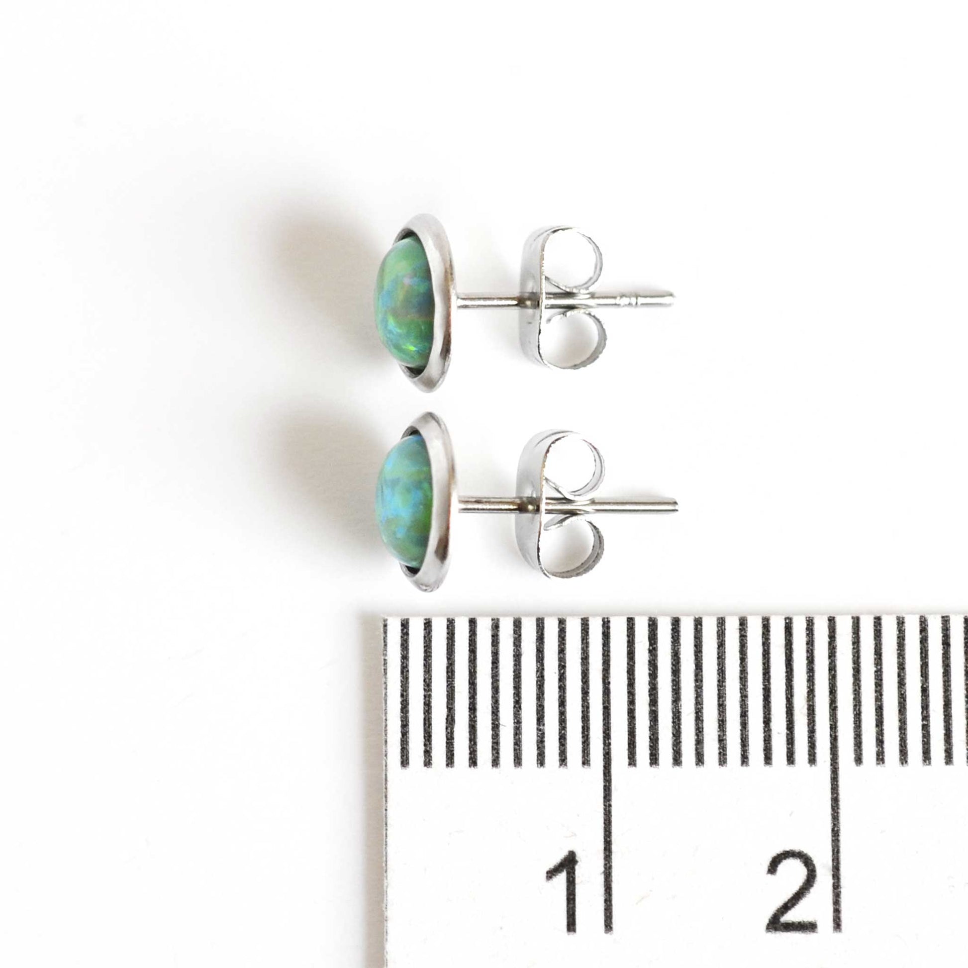 8mm diameter green lab Opal stud earrings next to ruler